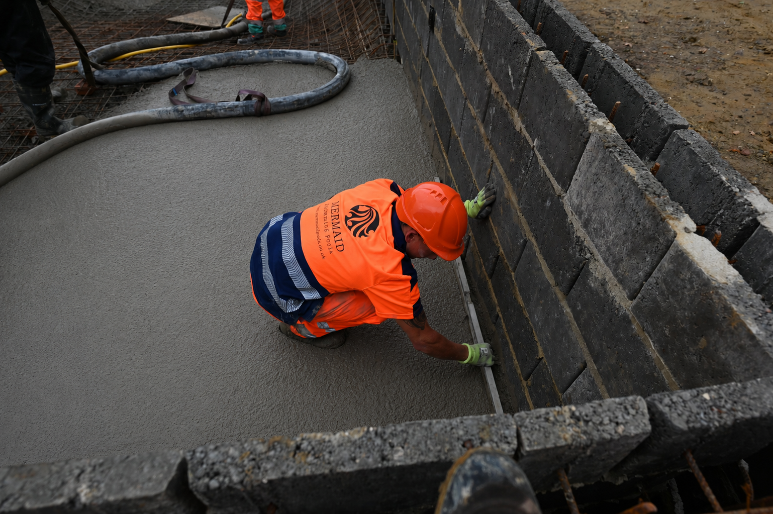 A Mermaid worker in branded workwear finishing a newly laid concrete pool floor