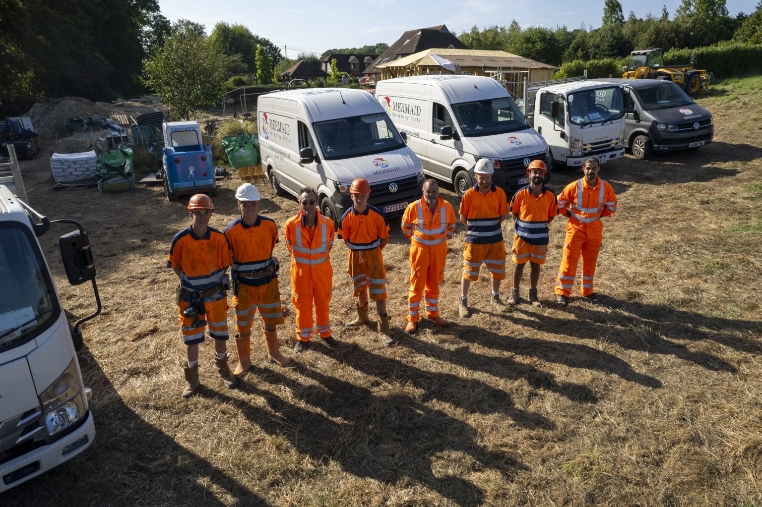 Eight members of the Mermaid construction team in workwear beside their branded vans on site